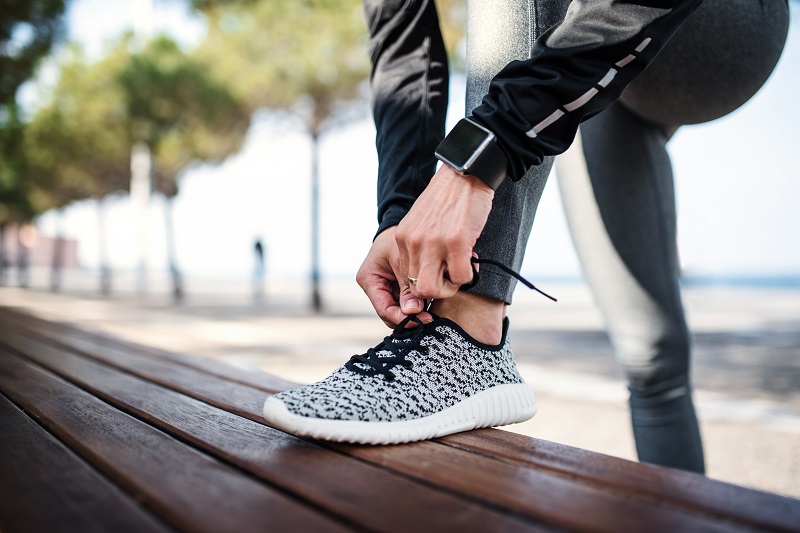 A young sportswoman with smartwatch outdoors in city, tying shoelaces.