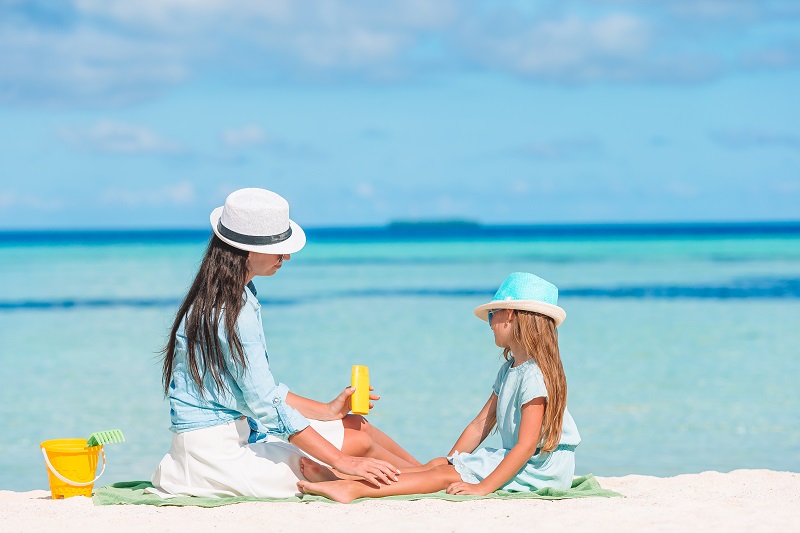 Young mother applying sun cream to daughter nose on the beach. Sun protection